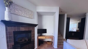 Ein Wohnzimmer mit Kamin, einem Fernseher auf einem Holzboden, einer Couch und einer Treppe, die zur Küche führt.