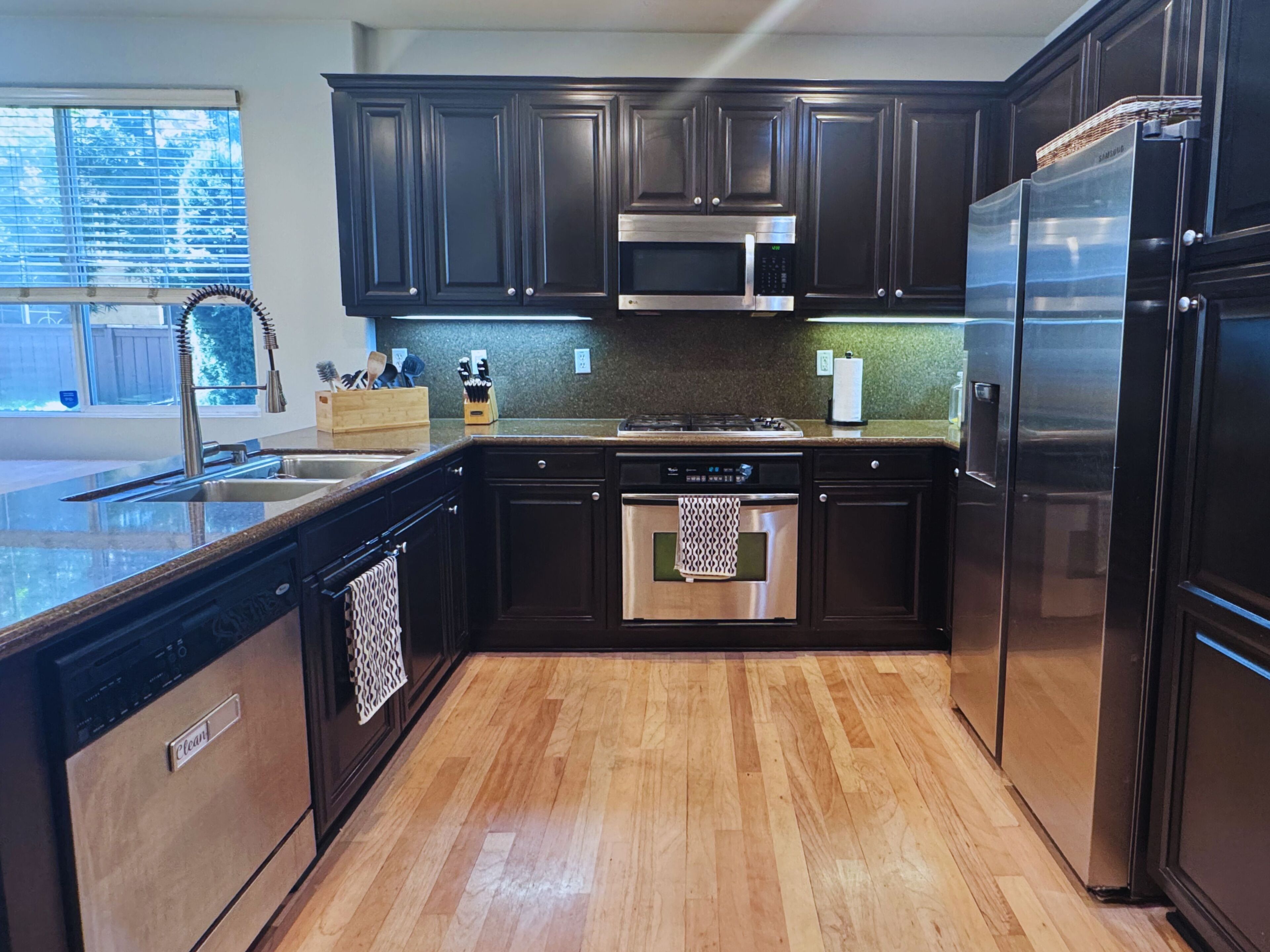 Une cuisine moderne avec des meubles de couleur sombre, des appareils électroménagers en acier inoxydable et un plancher en bois.