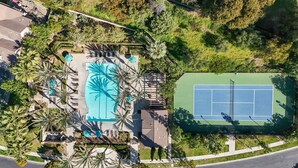 Luftaufnahme eines Resorts mit Schwimmbad, Tennisplatz und Palmen.