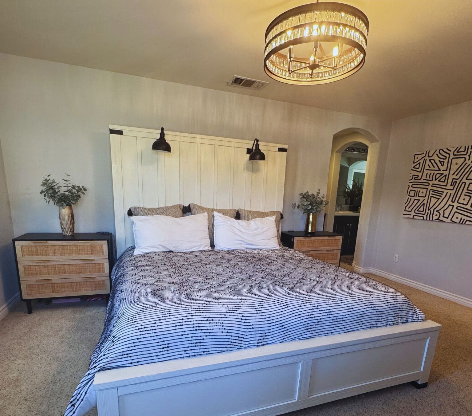 Une chambre à coucher avec un grand lit, deux tables de chevet, un lustre et un miroir.