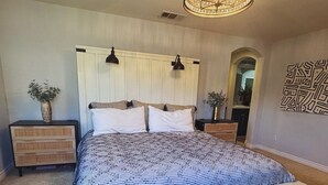 Ein Schlafzimmer mit einem großen Bett, zwei Nachttischen, einer Chandelüster und einem Spiegel.