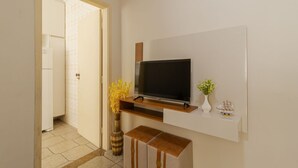 Et moderne værelse med et fladskærms-tv monteret på væggen, en lille træhylde nedenunder, en vase med blomster og en skibsmodel.