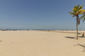 Een strand met een palmboom, heldere lucht en vakantiegangers in de verte.