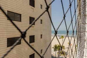 A building with a grid-patterned facade and a view of a beach with umbrellas and palm trees. - Apartamento Pet Friendly Beira-Mar no Guilhermina (Praia Grande)