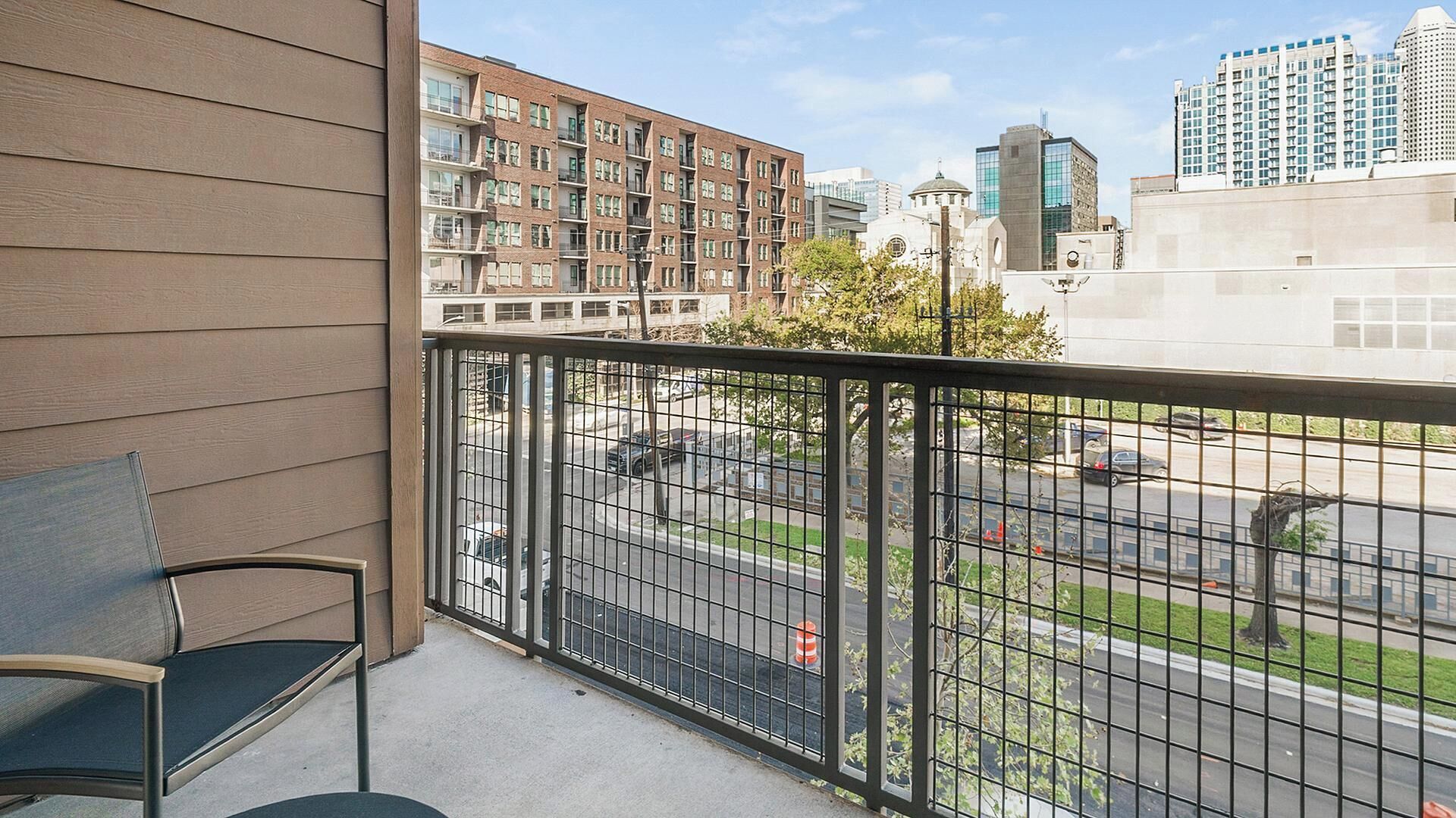 A balcony with a view of a city street, a chair, and a building with multiple floors.
