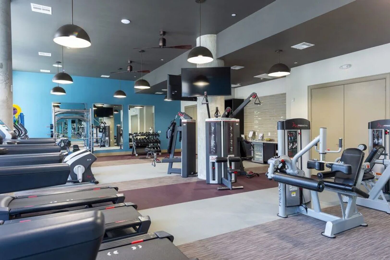 Une salle de sport équipée de tapis de course, d’appareils de musculation et de poids libres.