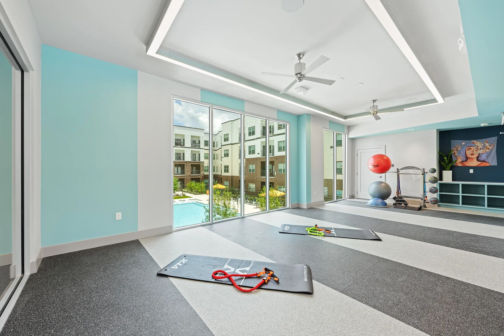 A modern gym with exercise mats, a ceiling fan, and a view of a swimming pool.