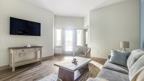 Una sala de estar con un televisor de pantalla plana, un sofá, una mesa de centro, una silla y una lámpara.