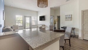 Una cocina moderna con encimeras de granito, un comedor con mesa y sillas, un televisor montado en la pared y una puerta con panel decorativo.