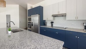 Een moderne keuken met granieten aanrechtbladen, roestvrijstalen apparatuur en blauwe kastjes.
