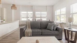 Ein modernes Wohnzimmer mit einem grauen Sofa, einem runden Couchtisch und einer Lampe auf einem Beistelltisch.