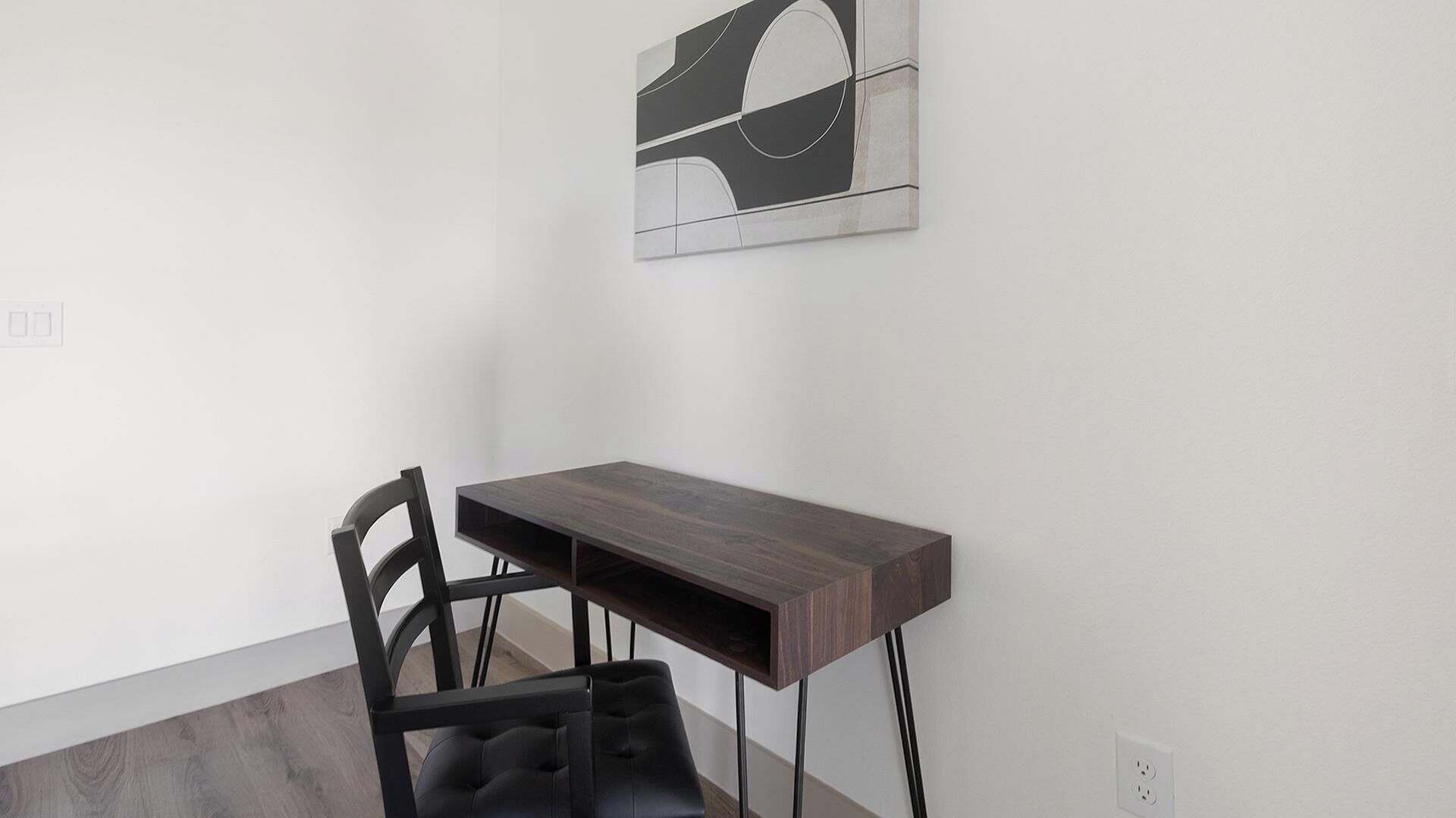 A modern room with a dark wooden desk, a black chair, and a minimalist abstract painting on the wall.