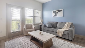 A living room with a sofa, armchair, coffee table, and artwork on the wall. - Landing | Modern 1BD, Courtyard, Yoga Studio (Houston)