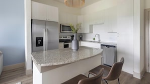 A modern kitchen with a granite countertop, stainless steel appliances, and a central island with seating. - Landing | Modern 1BD, Courtyard, Yoga Studio (Houston)