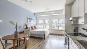 Een moderne hotelkamer met een bed, een eethoek, een keuken en grote ramen.