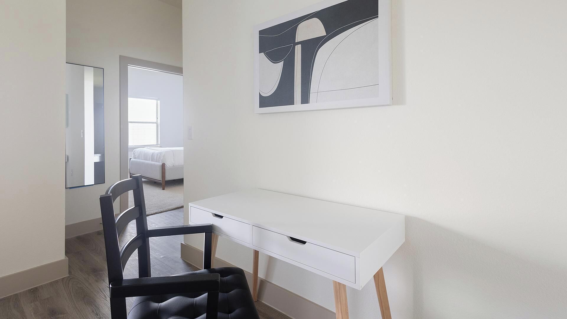 A modern bedroom with a white desk, a black chair, and a bed with white bedding.