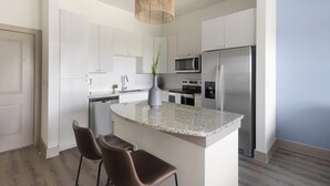Una cucina moderna con mobili bianchi, un'isola con piano in granito, elettrodomestici in acciaio inossidabile e una poltrona in pelle marrone.