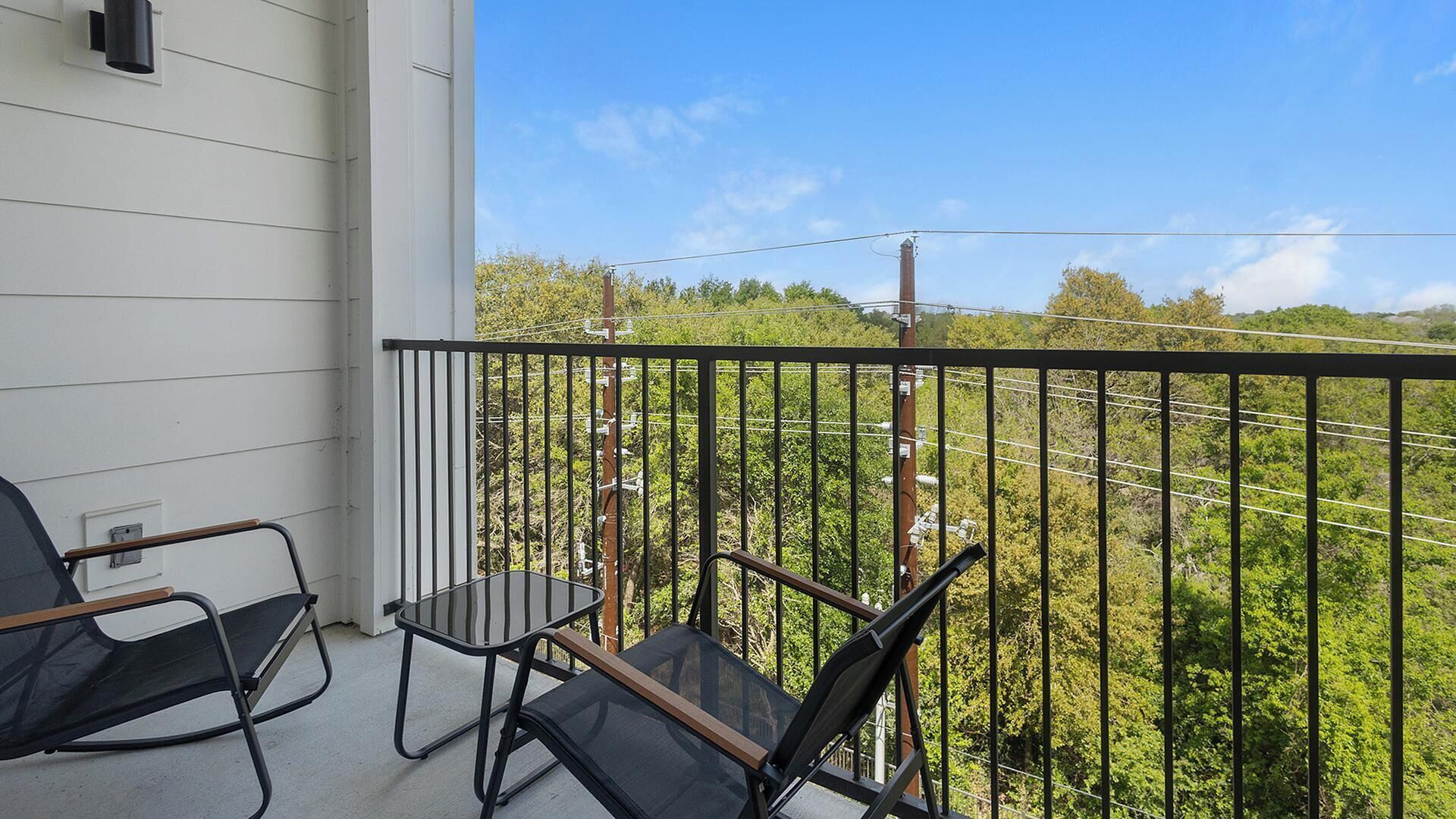 A balcony with two chairs and a table, overlooking a green landscape with power lines.