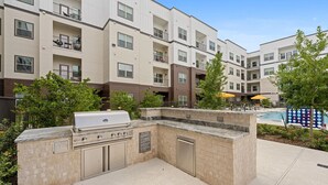 Um edifício de apartamentos moderno com área de churrasco, piscina ao ar livre e um pequeno jardim.