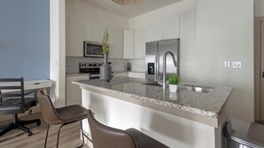 Cozinha moderna com bancada de granito, eletrodomésticos de aço inoxidável e um espaço bar com duas cadeiras.