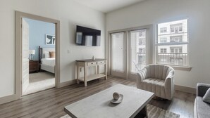 Uma sala de estar moderna com um sofá, uma mesa de centro, uma televisão, um armário e uma porta que dá para outro espaço.