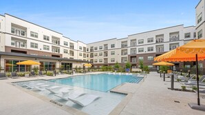 Piscina com espreguiçadeiras e guarda-sóis, cercada por edifícios altos.