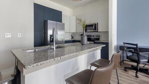 A modern kitchen with granite countertops, stainless steel appliances, and a bar area with leather chairs. - Landing | Chic 1BD, Courtyard, Yoga Studio (Houston)
