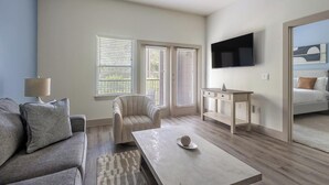 A modern living room with a sofa, armchair, coffee table, TV, and a desk. - Landing | Chic 1BD, Courtyard, Yoga Studio (Houston)