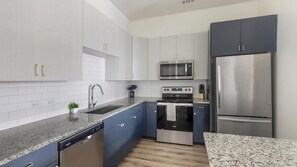 A modern kitchen with white cabinets, stainless steel appliances, and a granite countertop. - Landing | Chic 2BD, Courtyard, Gym (Houston)