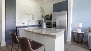 A modern kitchen with a granite countertop, stainless steel appliances, and a central island with seating. - Landing | Incredible 1BD, Courtyard, Gym (Houston)