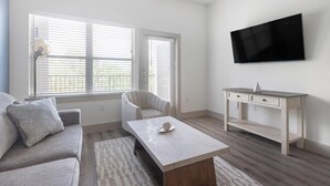 A living room with a sofa, a coffee table, a chair, a desk, and a TV mounted on the wall. - Landing | Incredible 1BD, Courtyard, Gym (Houston)