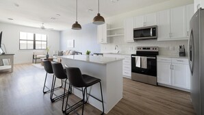 A modern kitchen with white cabinetry, a central island with bar stools, a microwave, oven, and refrigerator. - Landing | Modern 1BD, Clubhouse, Gym (Austin)