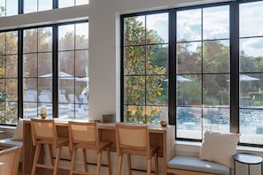 A dining area with a table and chairs, large windows with a view of a pool and outdoor seating. - Landing | Incredible 1BD, Gym, Clubhouse (Austin)