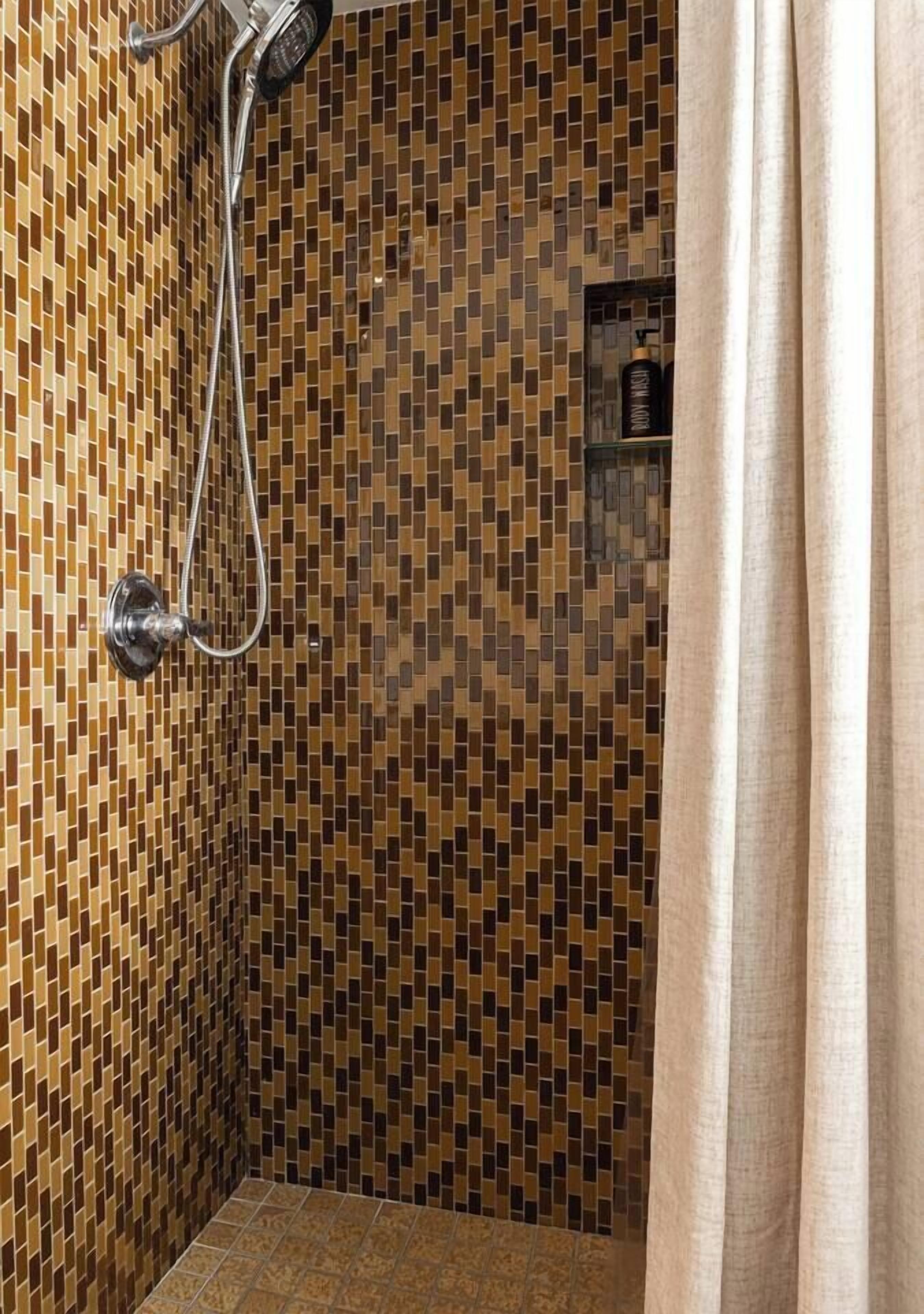 Eine Dusche mit Wand aus Mosaikfliesen und Duschkopf.