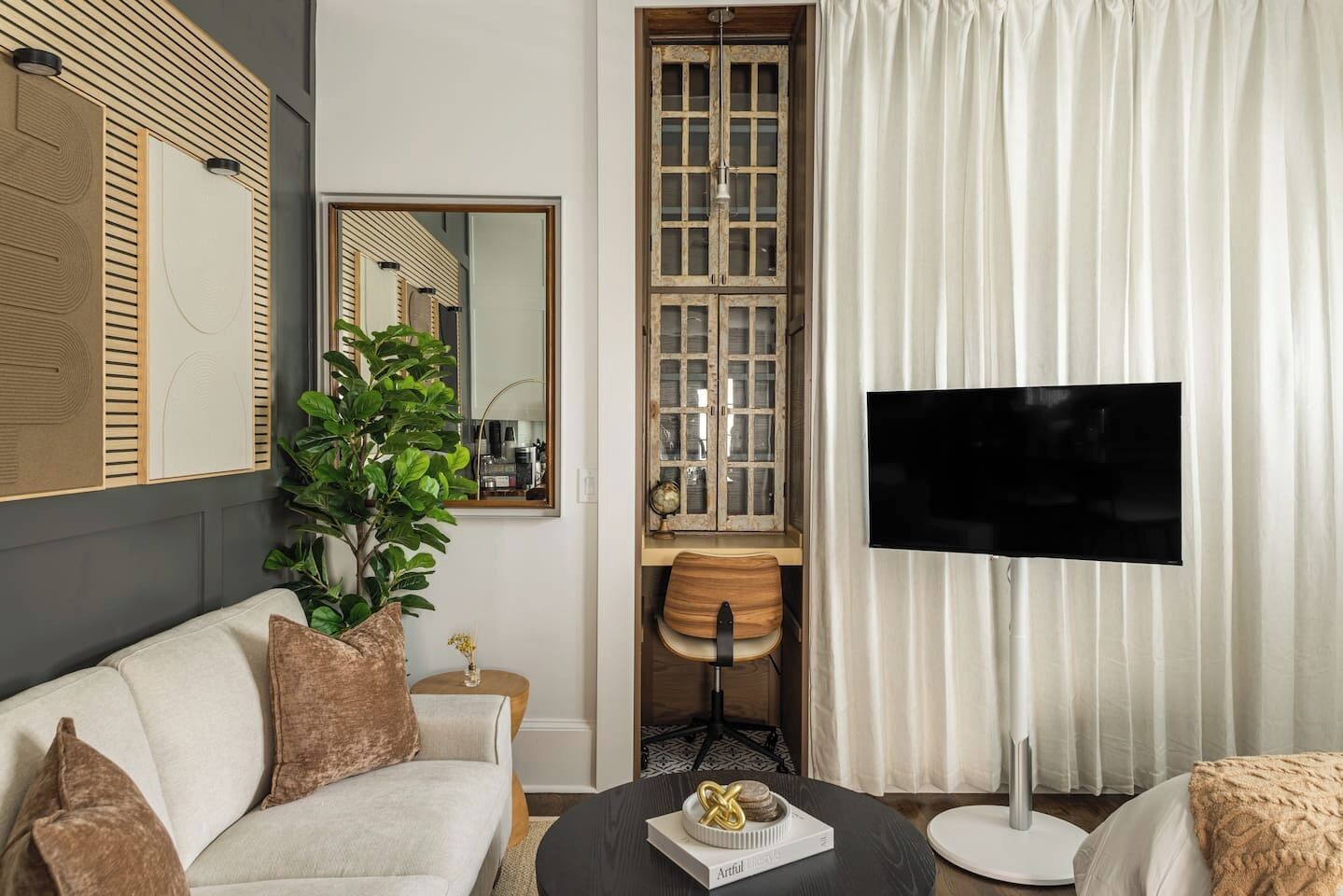 A modern living room with a sofa, a coffee table, a TV, a plant, and a cabinet with a mirror.