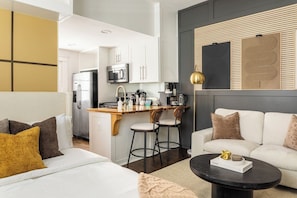 Ein modernes Wohnzimmer mit Sofa, Couchtisch und Küchenzeile mit Kühlschrank, Mikrowelle und Barhocker.