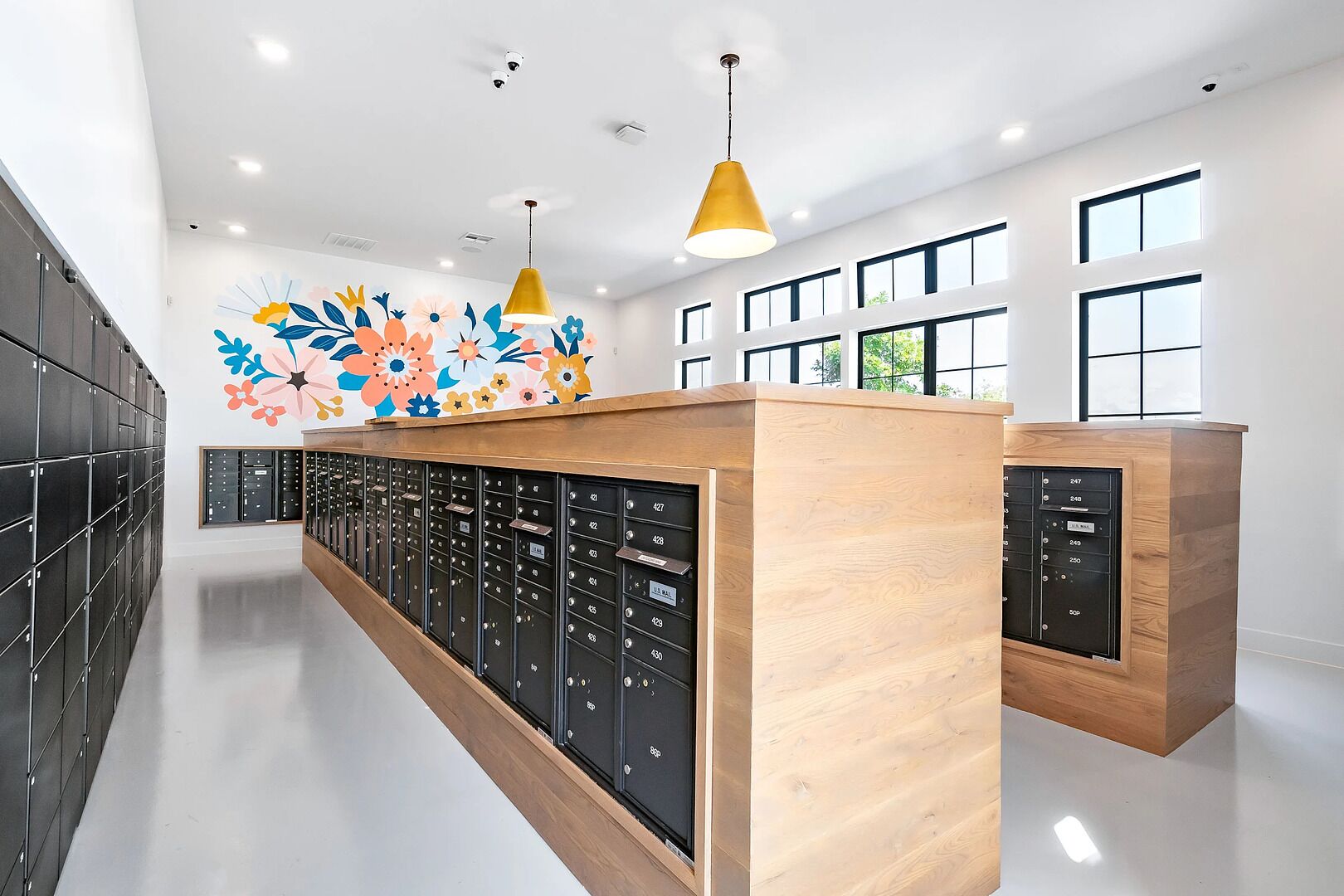 A modern hotel lobby with a long row of lockers, a wooden reception desk, and a colorful floral mural on the wall.