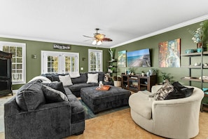 A living room with a sectional sofa, a chaise lounge, a ceiling fan, and artwork on the walls. - Living the Dream at Palm Estate Retreat (Surfside Beach)