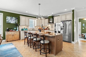 A kitchen with a central island, bar stools, a refrigerator, and a dining area. - Luxury Oceanfront Escape w/ Spa & Chef's Kitchen (Surfside Beach)