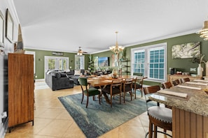 A spacious living area with a dining table, chairs, a sofa, and a kitchen in the background. - Living the Dream at Palm Estate Retreat (Surfside Beach)