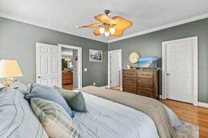 Une chambre à coucher avec un lit, un ventilateur de plafond, une commode et un téléviseur.