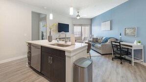 Una cocina moderna con una isla grande, una zona de comedor con un sofá y un escritorio, y una sala de estar con una pared azul de acento.