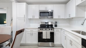 A modern kitchen with white cabinets, a stainless steel microwave, a stove, and a sink. - Landing | Modern 2BD, Gym, Clubhouse (Kissimmee)