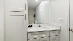 Une salle de bain avec un lavabo blanc, un miroir et des armoires.