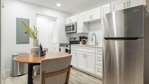 Une cuisine moderne avec des meubles blancs, des appareils en acier inoxydable et un coin repas comprenant une table et des chaises.