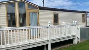 A mobile home with a white deck, large windows, and a chimney. - Happy Days Caravan Park - Holiday Accommodation 21912 (Abergele)
