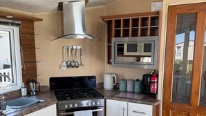 A compact kitchen with a stove, oven, microwave, and wooden cabinets. - Happy Days Caravan Park - Holiday Accommodation 21912 (Abergele)