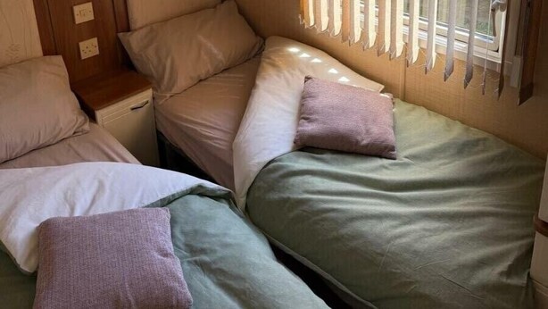 A compact room with bunk beds, a small cabinet, and a window with vertical blinds. - Happy Days Caravan Park - Holiday Accommodation 21912 (Abergele)