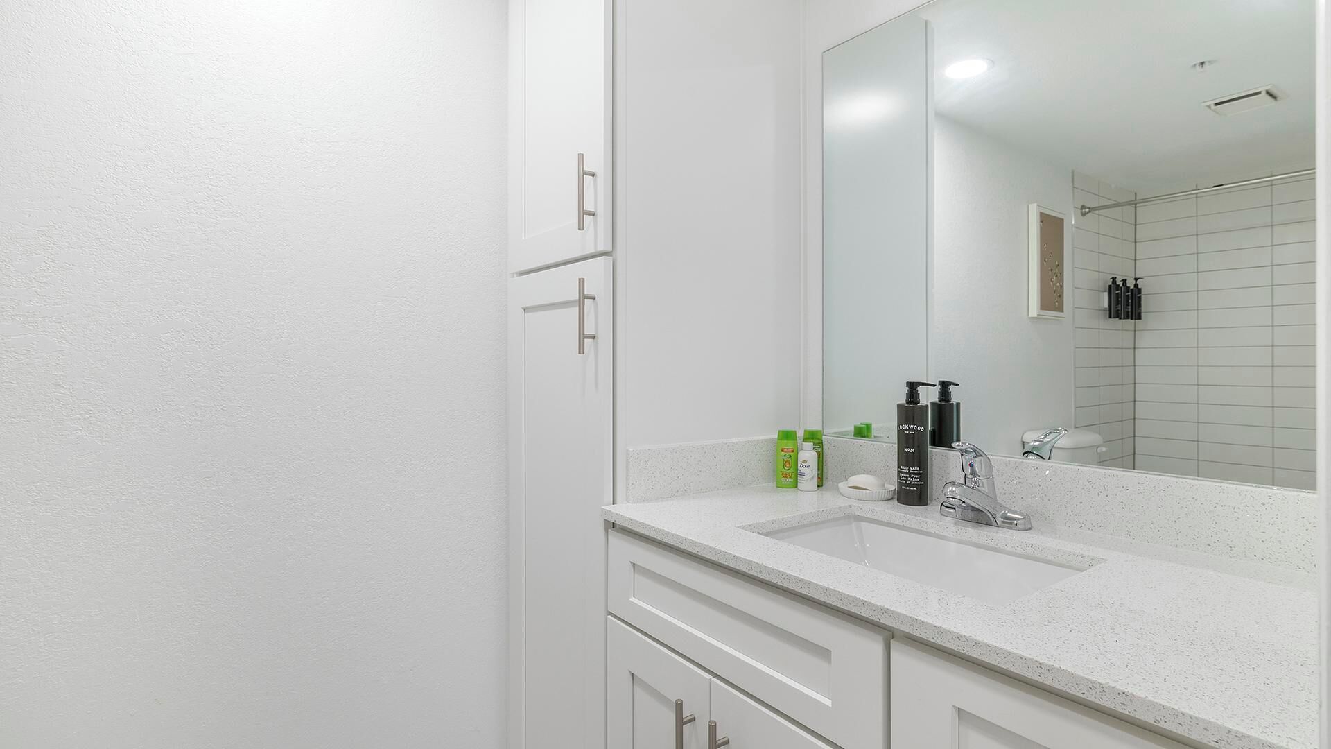 Une salle de bain moderne avec un plan de toilette blanc, un grand miroir et un espace douche.