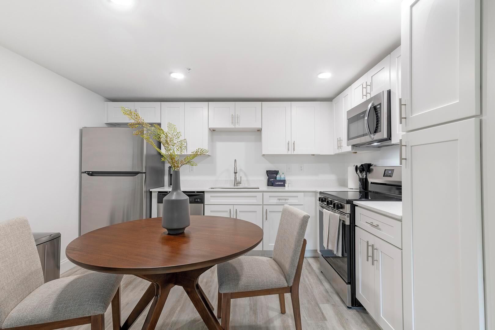 A modern kitchen with white cabinets, stainless steel appliances, and a round wooden table with chairs.